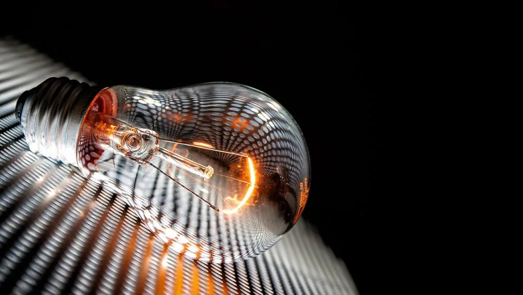 Uma lâmpada acesa apoiada sobre um painel fotovoltaico, simbolizando a relação entre energia solar e iluminação sustentável no contexto do TCC Engenharia Elétrica.