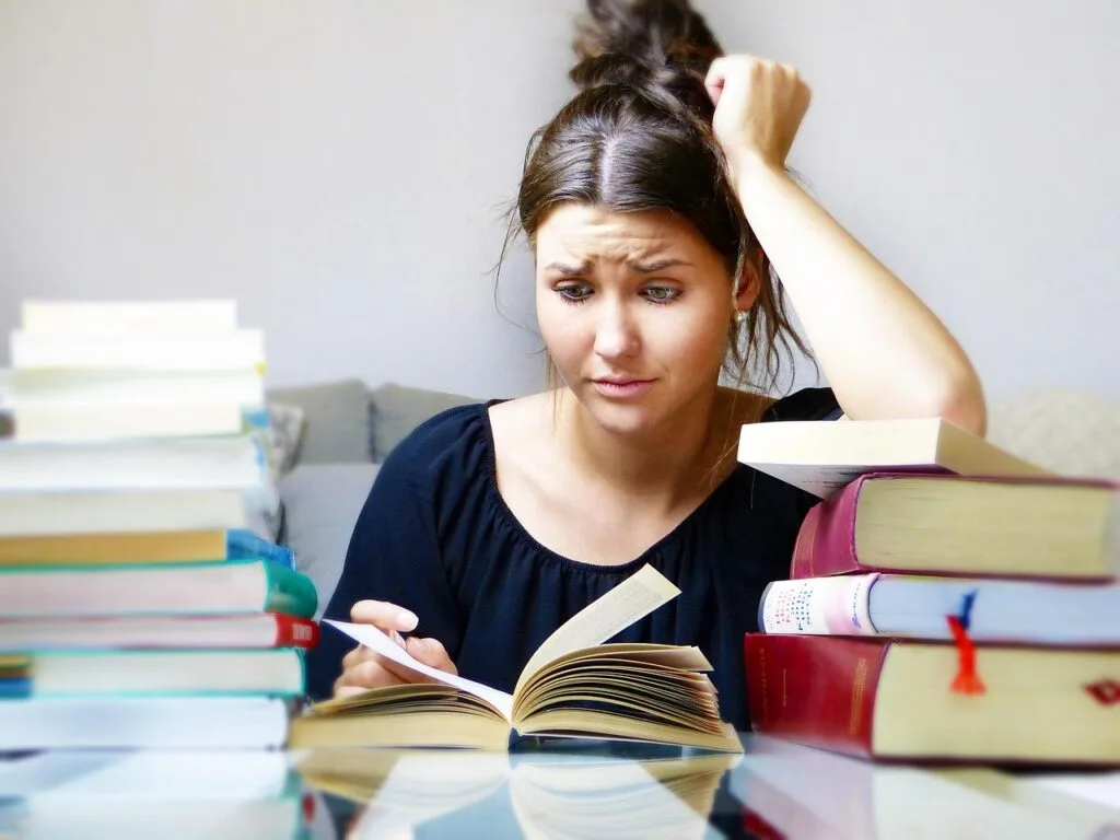 Estudante de engenharia cercada por uma pilha de livros, se preparando para o TCC Engenharia, com foco em temas de Engenharia de Produção, Mecânica e Elétrica.