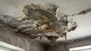 Infiltração na laje de concreto com mancha escura, tinta descascada e ferrugem no teto de uma casa